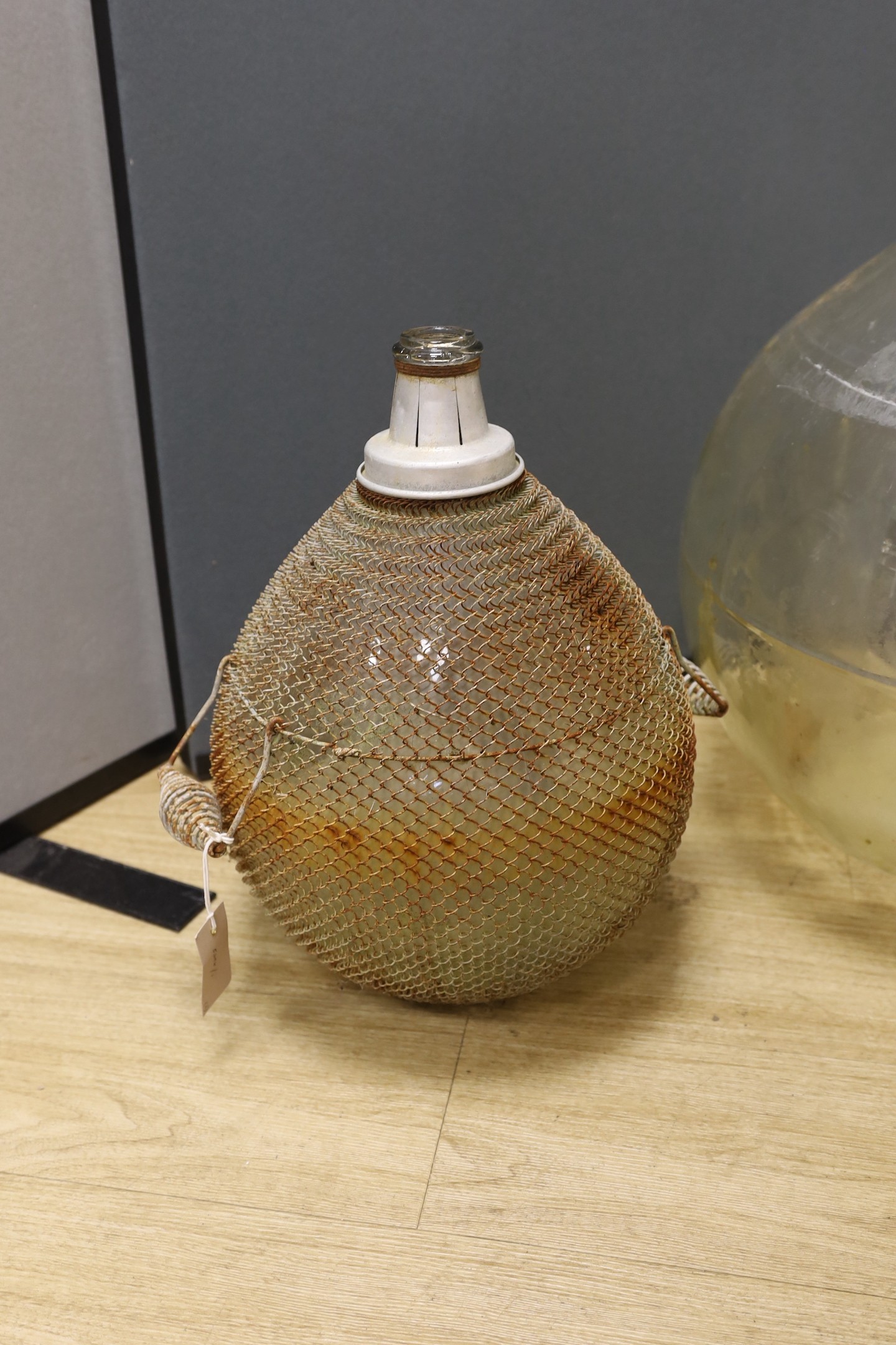 A large clear glass carboy and unusual wire-mounted glass carboy, largest 28cms high.